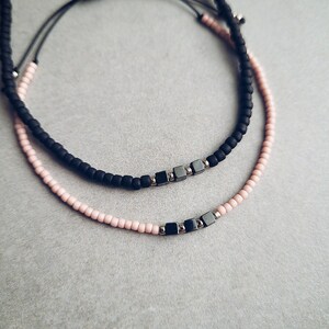 May include: Two beaded bracelets, one black and one pink, with silver metal square beads.