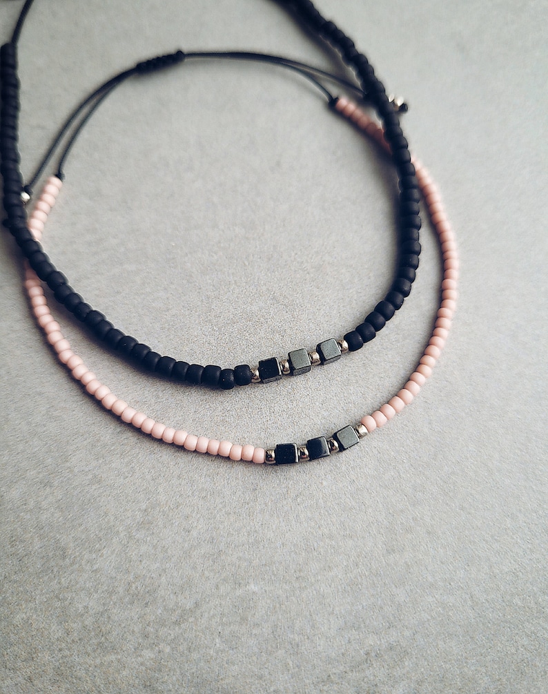 May include: Two beaded bracelets, one black and one pink, with silver metal square beads.