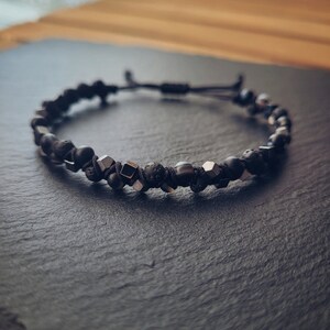 May include: A black beaded bracelet with silver accents. The bracelet is made with black lava rock beads, black onyx beads, and silver metal beads.