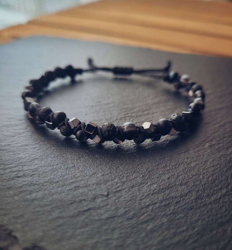 May include: A black beaded bracelet with silver accents. The bracelet is made with black lava rock beads, black onyx beads, and silver metal beads.