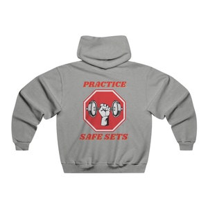 Könnte beinhalten: Grauer Kapuzenpullover mit einem roten Stoppschild-Motiv, das eine Hand zeigt, die eine Hantel hebt. Der Text "PRACTICE SAFE SETS" ist in Rot und Orange gedruckt.