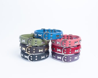 May include: A stack of colorful leather dog collars with silver bone-shaped accents. The collars are arranged in a circle, with the blue collar on top.