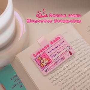 Könnte beinhalten: Doppelseitige magnetische Lesezeichen mit einem rosafarbenen Bibliothekskartendesign mit einer Comic-Hundfigur. Die Karte trägt die Aufschrift "Library Card" und "Top Notch Reader".