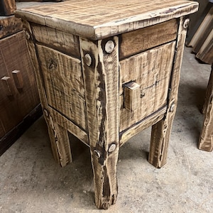 Könnte beinhalten: Ein rustikaler Nachttisch aus Holz mit einer Schublade und einer kleinen Tür. Der Nachttisch ist aus hellem und dunklem Braunholz gefertigt und hat eine Used-Optik. Der Nachttisch ist ca. 61 cm hoch, 46 cm breit und 41 cm tief.