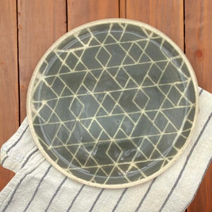May include: A round ceramic plate with a gray background and a white geometric pattern. The plate has a slightly raised rim.