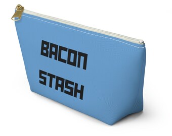 Könnte beinhalten: Hellblaue Reißverschlusstasche mit dem schwarzen Schriftzug "BACON STASH". Der Reißverschluss ist goldfarben, und am oberen Rand befindet sich eine weiße Naht.