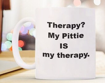 May include: White ceramic coffee mug with black text that reads "Therapy? My Pittie IS my therapy."