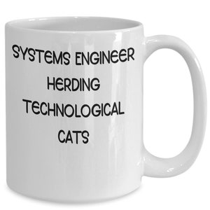 May include: White ceramic coffee mug with black text that reads "Systems Engineer Herding Technological Cats".