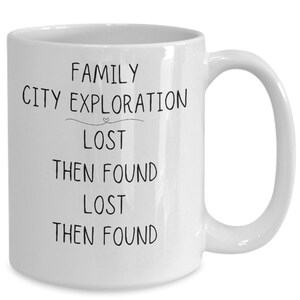 May include: White ceramic coffee mug with black text that reads "Family City Exploration Lost Then Found Lost Then Found".