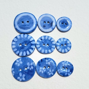 May include: Assortment of blue ceramic buttons with white designs. Some buttons have a simple white circle design, while others have a more intricate floral pattern.