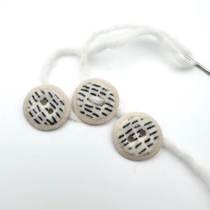 Op de afbeelding: Een set van drie keramische mokken met een gespikkelde, matte afwerking. De mokken zijn in de kleuren crème, lichtgrijs en donkergrijs. Elke mok heeft een eenvoudig, minimalistisch ontwerp en een afgeronde handgreep.