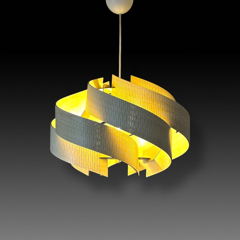 May include: A modern pendant light fixture with a spiral design. The light has a white ceiling mount and a series of gray and yellow curved bands. The bands are made of a perforated material that allows light to shine through. The light is suspended from the ceiling by a white cord.
