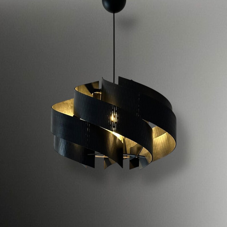 May include: A modern black pendant light with a spiral design. The light fixture has a series of curved, black panels that create a layered effect. The interior of the panels is a warm gold color, and a single light bulb is visible.