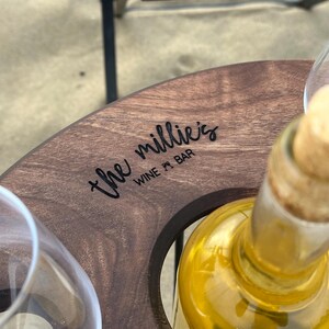 May include: A wooden wine bottle holder with two glass cups and the text "the millie's WINE + BAR" engraved on the top.
