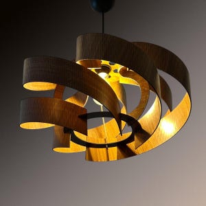May include: A modern, spiral-shaped pendant light fixture. The fixture features curved, wooden slats in a dark brown color, creating a layered, open design. The interior reveals a warm, golden glow from the light source, creating a dramatic effect. The fixture is suspended from a black ceiling mount.