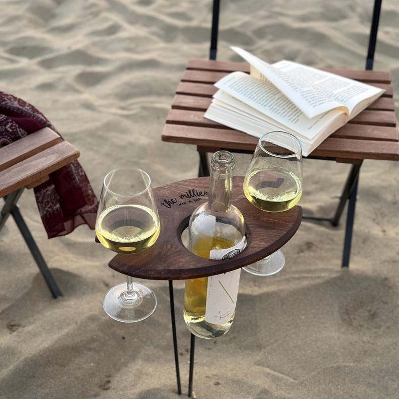 May include: A wooden wine holder with two glass wine glasses and a bottle of wine. The holder is engraved with the words "the millies wine + fun".