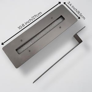 Op de afbeelding: Een rechthoekige, donkergrijze metalen vuurkorfbrander met een gaasinterieur. De brander is 27 cm lang en 8,5 cm breed. Een bijpassende metalen pook is inbegrepen.