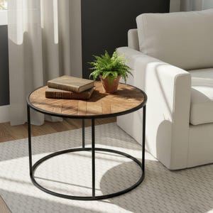 May include: A round side table with a black metal frame and a wooden top. The tabletop has a herringbone pattern. A small potted plant and two books sit on the table. The table is near a white sofa.
