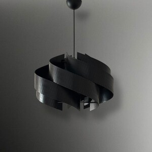 May include: A modern black pendant light with a unique, swirling design. The light fixture is suspended from a black cord and features layered, curved wooden slats. The overall shape is reminiscent of a spiral or a stylized flower.