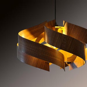 Op de afbeelding: Een moderne houten hanglamp met een uniek, wervelend ontwerp. De lamp is gemaakt van gebogen, getextureerde houten stroken, waardoor een gelaagd effect ontstaat. Het warme licht van binnenuit verlicht de houtnerf en voegt een gezellige sfeer toe.
