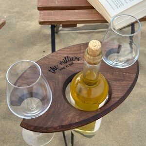 May include: A wooden wine and glass holder with a cutout for a bottle and two glasses. The holder is engraved with the text "the millie's WINE + BAR".