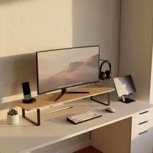 May include: A modern home office setup featuring a large computer monitor on a wooden stand with black metal legs. A wireless keyboard, mouse, and headphones are also visible. A smartphone, a laptop, and a small potted plant complete the workspace.