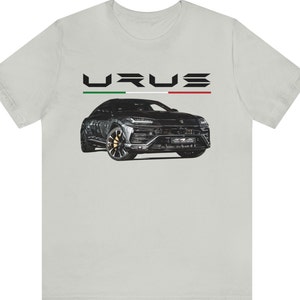 May include: A white t-shirt with a black and grey Lamborghini Urus printed on the front. The car is surrounded by a black and white Italian flag.
