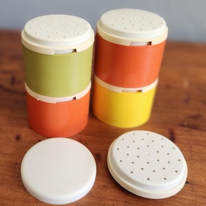 Puede incluir: Juego de cuatro especieros vintage en colores brillantes: verde, naranja y amarillo. Cada especiero tiene una tapa blanca con pequeños agujeros. Dos tapas están separadas. Los especieros son cilíndricos y de plástico.