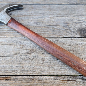 May include: A claw hammer featuring a polished silver-toned metal head with a curved claw and a smooth, cylindrical wooden handle with a rich brown finish. The tool is designed for driving nails and removing them with the integrated claw feature.