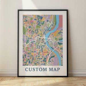 Könnte beinhalten: Ein gerahmter, individueller Kartendruck mit einem farbenfrohen, abstrakten Design. Die Karte zeigt einen Fluss und einen Stadtplan in Blau-, Grün-, Rosa- und Gelbtönen. Der Text "CUSTOM MAP" ist unten in dunkelblauer Schrift gedruckt.