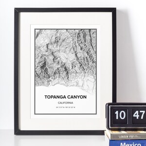 May include: A black and white topographic map print of Topanga Canyon, California. The print is framed in a black frame and includes the coordinates 34&deg; 3' 57" N 118&deg; 33' 32" W.