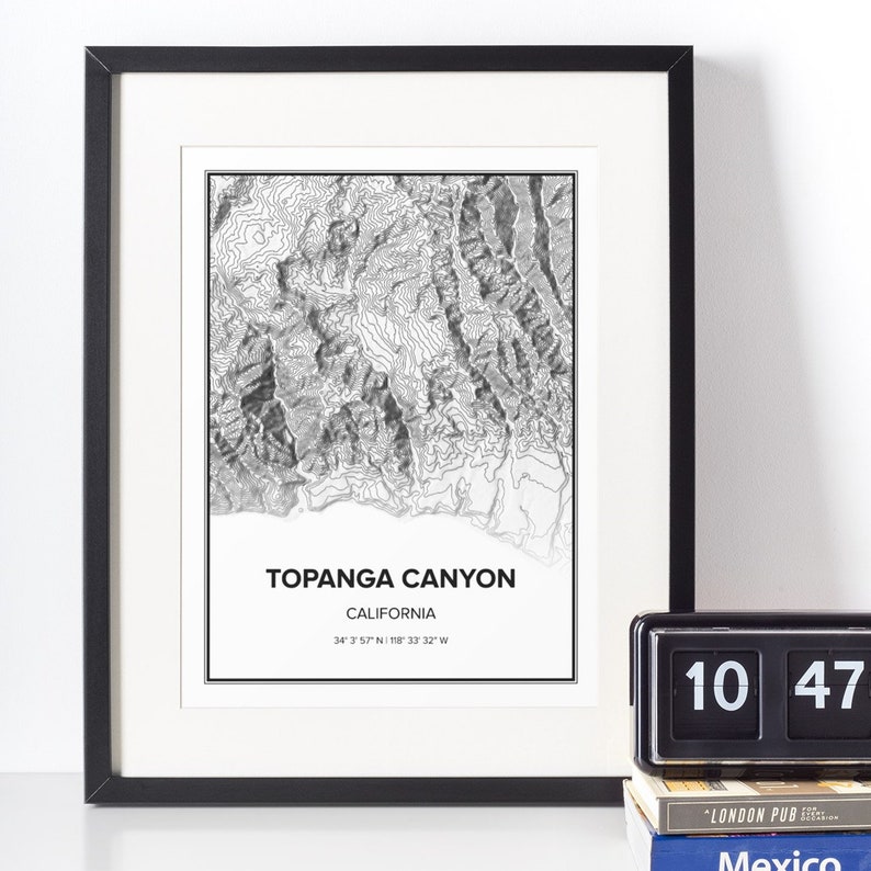 May include: A black and white topographic map print of Topanga Canyon, California. The print is framed in a black frame and includes the coordinates 34&deg; 3' 57" N 118&deg; 33' 32" W.