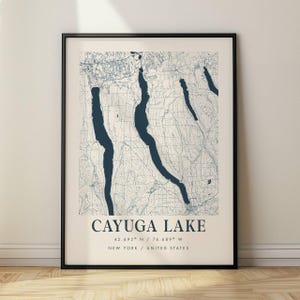 Può includere: Una stampa incorniciata della mappa del lago Cayuga a New York, Stati Uniti. La mappa presenta un design topografico dettagliato in blu e bianco, con la forma del lago ben visibile. Il testo "CAYUGA LAKE" è centrato in basso, con coordinate e dettagli sulla posizione.