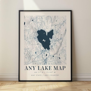 Puede incluir: Una lámina de arte enmarcada que muestra un mapa de lago en azul oscuro con líneas de contorno topográficas sobre un fondo crema claro. El texto dice ANY LAKE MAP, 44.11 N / 73.92 W y ANY STATE / ANY COUNTRY en una fuente azul oscuro sin remates.