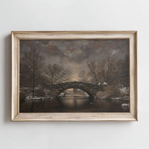 以下が含まれることがあります： 額縁に入った絵画で、暗い水面にかかる石橋のある冬の風景が描かれています。 裸の木と雪に覆われた茂みが土手を縁取っています。 空は曇っており、絵画は落ち着いた色使いです。