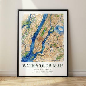 May include: A framed wall art print featuring a watercolour map of a city with blue waterways and tan land masses. The text reads WATERCOLOR MAP, 40.760°N / 73.970°W, and ANY STATE / ANY COUNTRY in a black serif font on a white background.