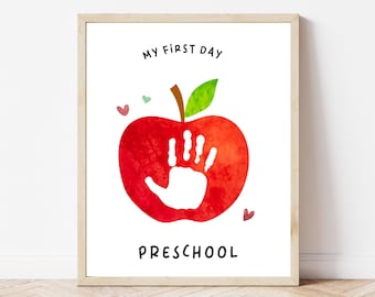 May include: A printable first day of preschool sign featuring a red apple with a white handprint inside. The text "My First Day Preschool" is written below the apple.