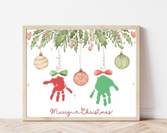 Pode incluir: Uma impressão de Natal emoldurada com uma guirlanda de azevinho verde e impressões de mãos vermelhas e verdes. As impressões de mãos têm a forma de ornamentos e têm os nomes "Noah" e "Emma" escritos acima. A impressão diz "Feliz Natal" na parte inferior.