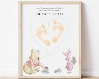 May include: A framed print featuring Winnie the Pooh and Piglet. The print includes a heart-shaped design with baby footprints and the text "IN YOUR HEART". The characters are surrounded by flowers and a ladybug.
