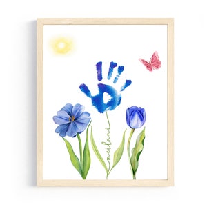 May include: A framed watercolor painting of a blue handprint with a blue flower and a purple tulip. The handprint is surrounded by green leaves and the name "milani" is written in cursive on the stem. A pink butterfly is flying above the flowers.