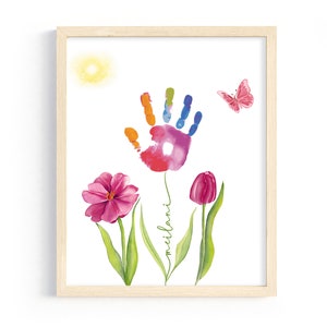 May include: A framed print with a colorful handprint surrounded by pink flowers and a butterfly. The print includes the name "Milan" written in cursive.