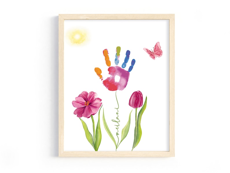 May include: A framed print with a colorful handprint surrounded by pink flowers and a butterfly. The print includes the name "Milan" written in cursive.