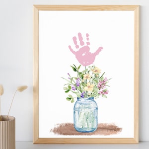 Könnte beinhalten: Ein rosa Handabdruck im Aquarell-Stil ist der Mittelpunkt dieses Drucks. Der Handabdruck ist als Blumenstiel mit einem Strauß bunter Blumen in einem durchsichtigen Glas dargestellt.