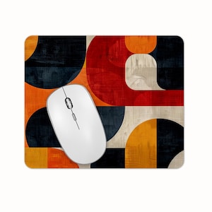 May include: A white wireless computer mouse sits on a rectangular mousepad. The mousepad has a geometric design with red, orange, black, and beige shapes. The design has a mid-century modern aesthetic.