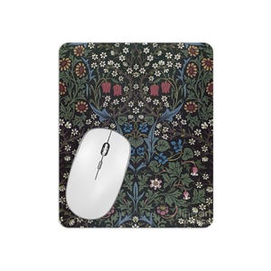 May include: A mouse mat with a floral pattern in shades of blue, green, red, and white. The pattern features stylised flowers, leaves, and stems. The mouse mat is rectangular and has a smooth surface.