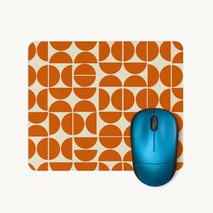 May include: A rectangular mouse pad featuring a repeating geometric pattern of orange semi-circles on a cream background, with a metallic blue computer mouse resting on the lower right side of the surface.