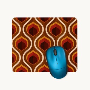 May include: A rectangular mouse mat featuring a repeating geometric pattern of interlocking ogee shapes in shades of brown, orange, and cream, with a bright blue computer mouse resting on the lower right corner of the surface.