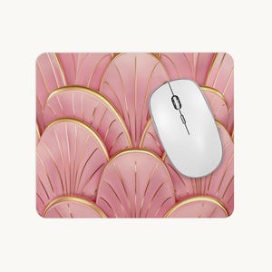 May include: A rectangular mouse mat featuring a repeating pattern of overlapping pink fan-shaped segments outlined in gold. A white wireless computer mouse with a central scroll wheel and two buttons is positioned on the right side of the mat.