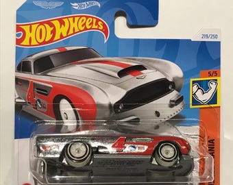 May include: A silver and red die-cast toy car, an Aston Martin DB4GT High-Speed Edition, on a blue and white Hot Wheels card. The car has a number "4" on the side and the words "Aston Martin DB4GT High-Speed Edition" are printed on the card. The card also has the Hot Wheels logo and the number 219/250.