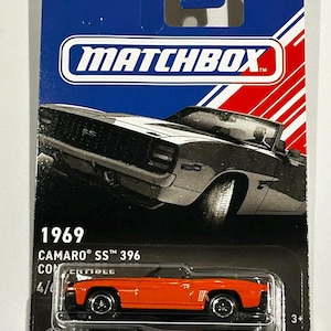 Op de afbeelding: Een Matchbox modelauto van een 1969 Camaro SS 396 cabriolet. De auto is oranje met zwarte accenten en staat op een zwart-blauwe kaart. De verpakking toont het Matchbox-logo en de tekst "Designed for a Lifetime."